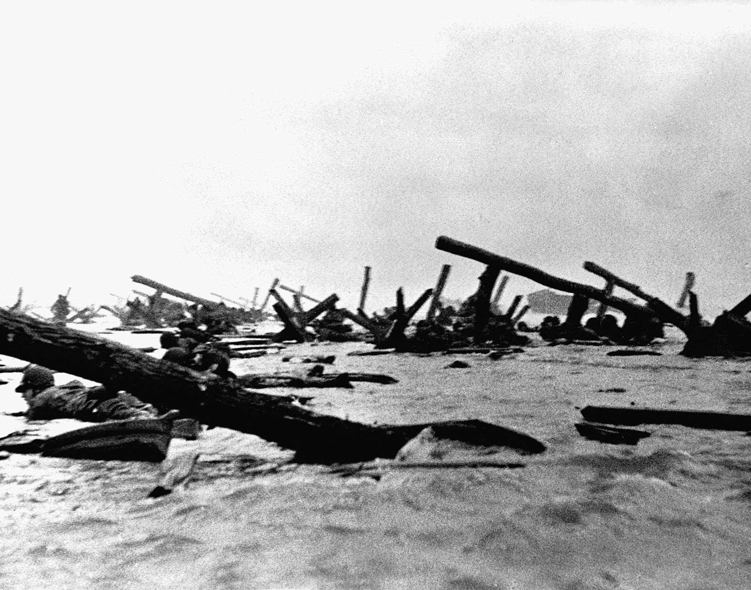 	Allied soldiers crawl on their stomachs past log fortifications.