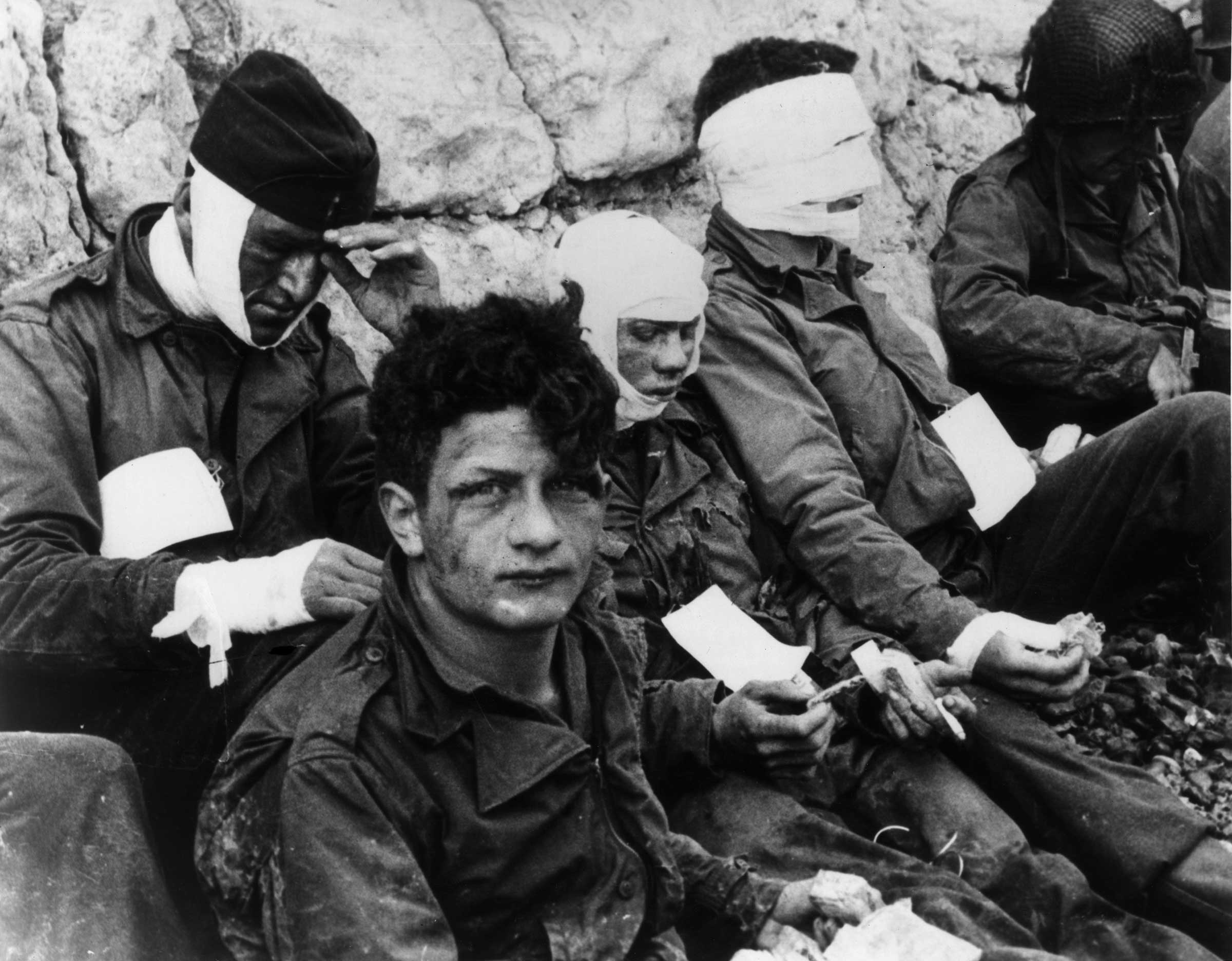 Wounded soldiers of the 3rd Battery, 16th Infantry Regiment, 1st US Infantry Division, lean against chalk cliffs.